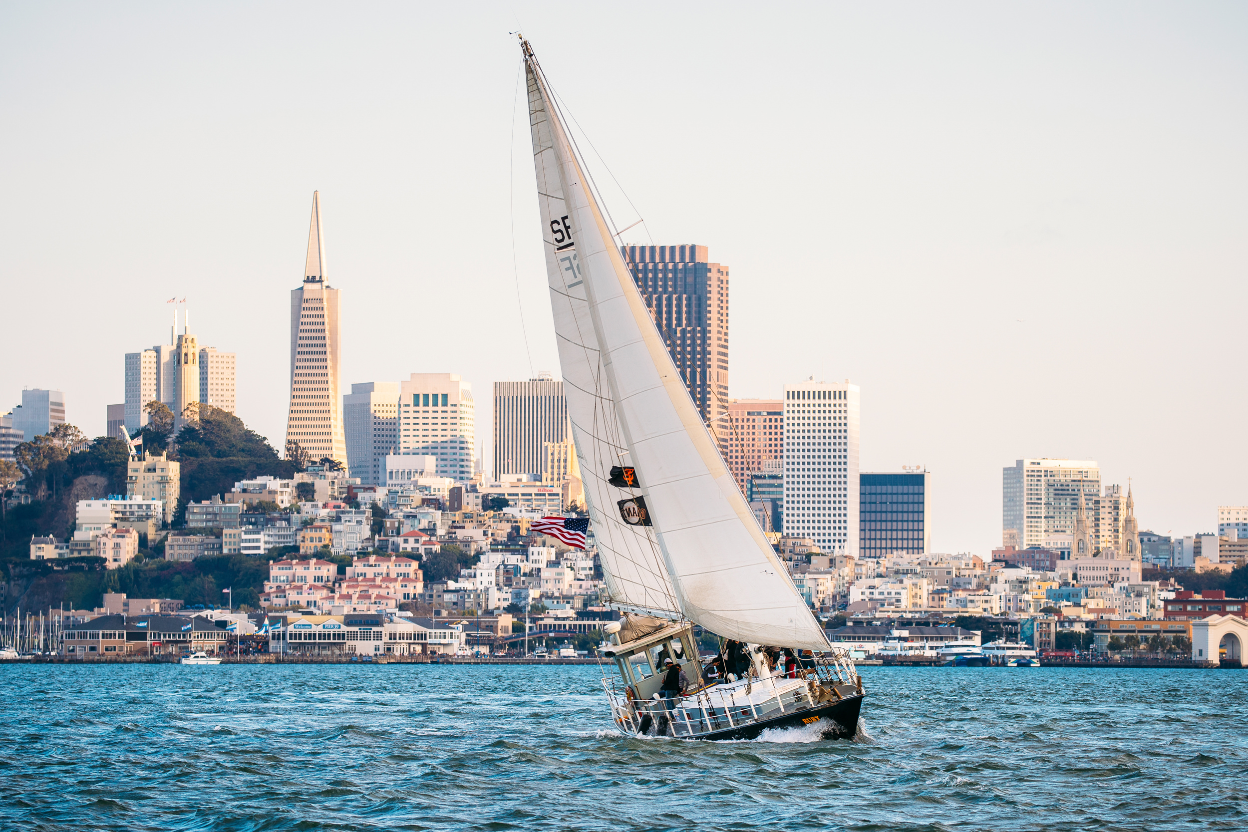 A sailboat sails on the sea with the city in the background