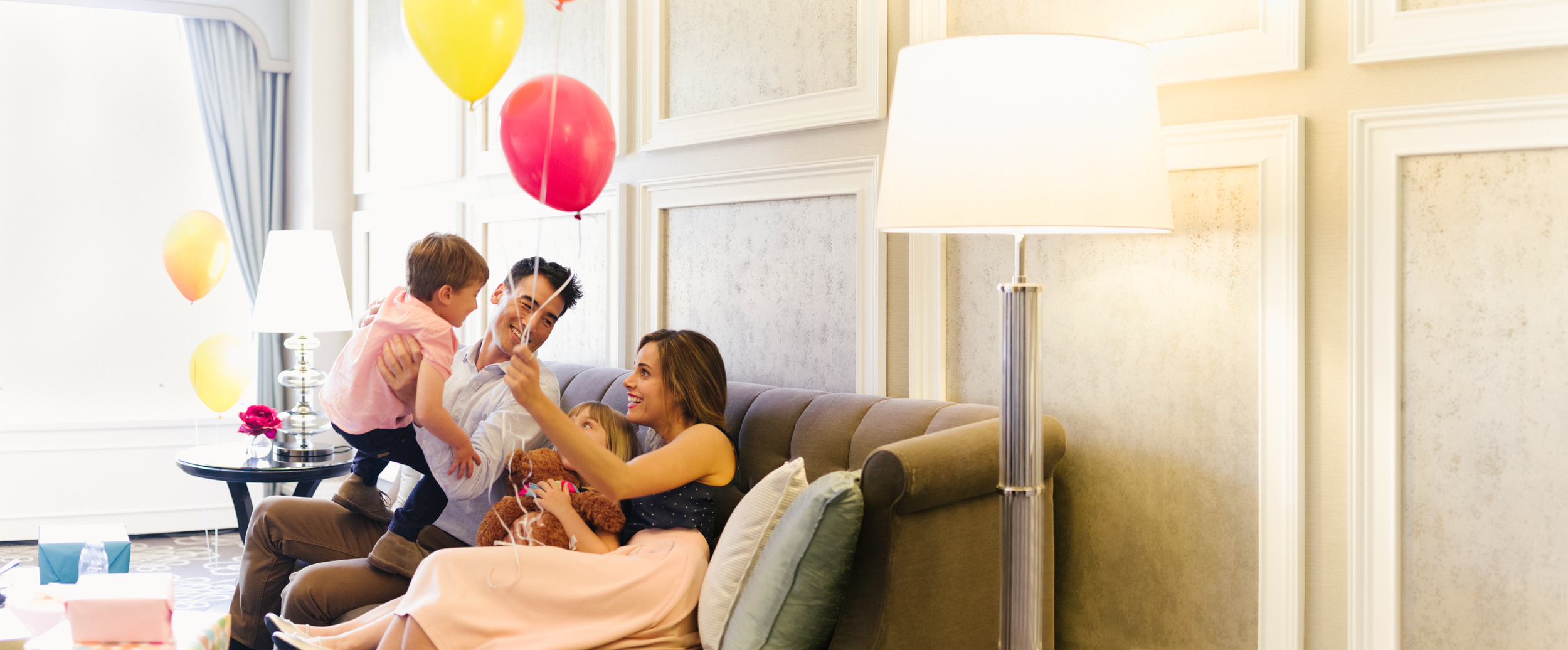 A family of four with balloons is on the sofa in the living room