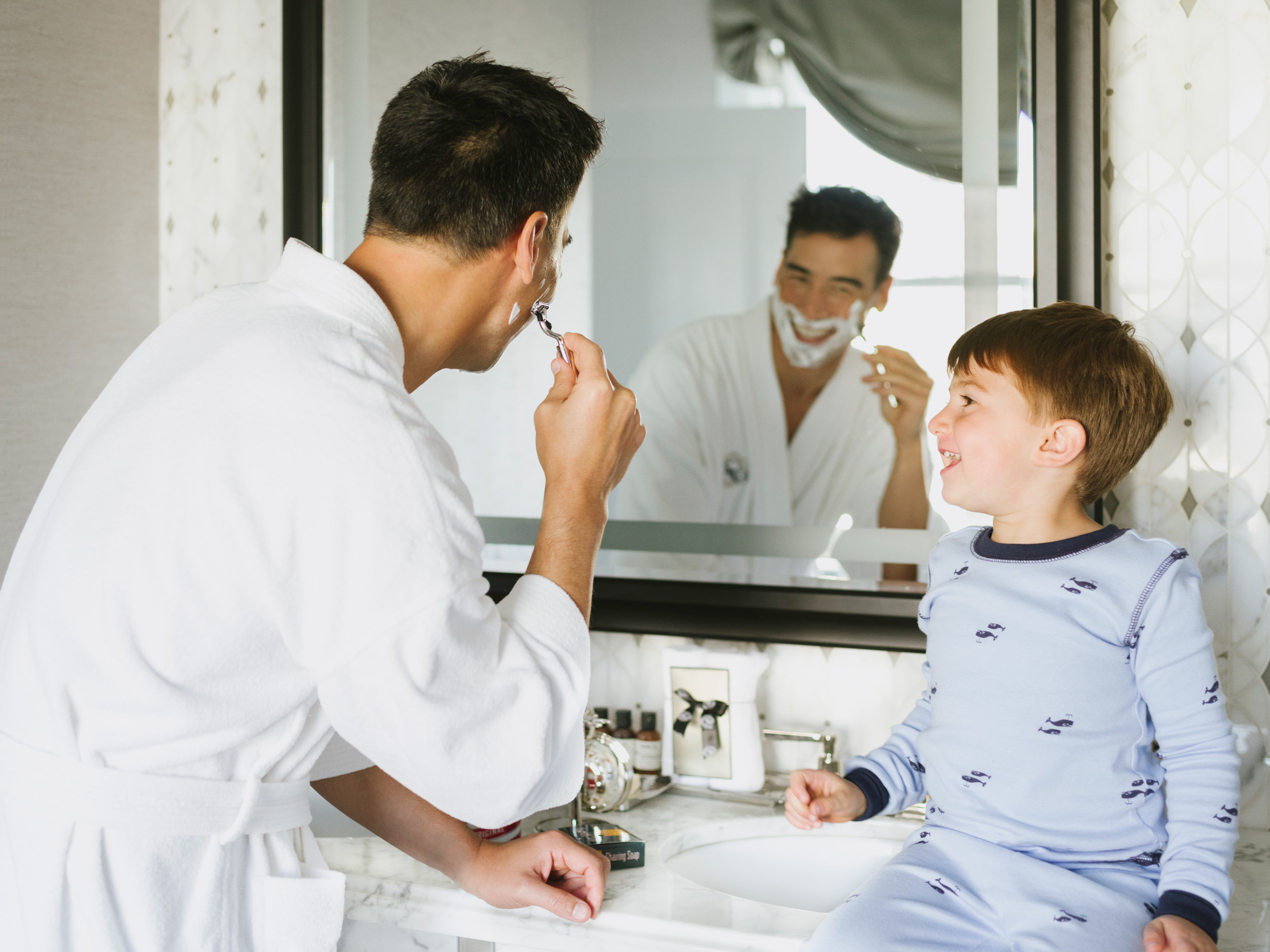 A shaving father and son are in the bathroom